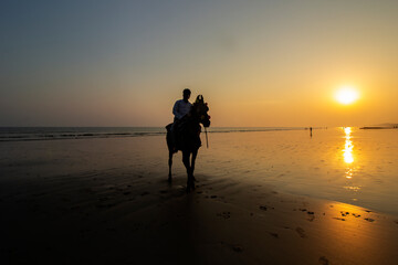 An young traveler riding horse on beach at sunset.