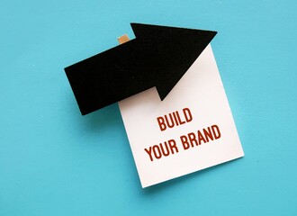 Black arrow direction on blue copy space background with text note BUILD YOUR BRAND, means entrepreneur differentiate service product from competition by creating  brand to attract customer perception