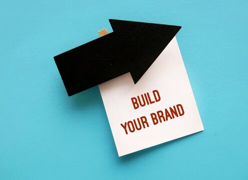 Black arrow direction on blue copy space background with text note BUILD YOUR BRAND, means entrepreneur differentiate service product from competition by creating  brand to attract customer perception