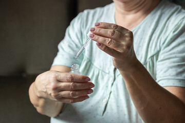 Senior woman hand holds pipette over glass bottle with facial vitamin serum or essential oil. Skincare and face care.