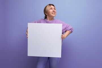 attractive blond woman holding a sheet of paper with a mockup for a promotion message on a purple background