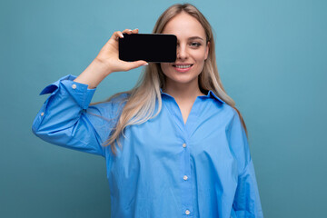 smiling informal blond girl holding smartphone with blank screen mockup for website on blue background