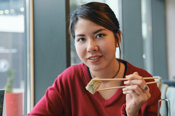 Young Asian girl eating sushi with chopsticks in a restaurant