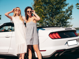 Two young beautiful and smiling hipster female in convertible car. Sexy carefree women posing near...