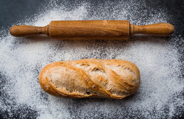 Fresh delicious bread, wooden rolling pin and flour close-up. Freshly baked bread baguette with a...