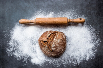 Fresh delicious bread, wooden rolling pin and flour close-up. Freshly baked sourdough bread with a golden crust. The context of a bakery with delicious bread. Confectionery products.