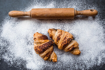 Delicious freshly baked croissants with chocolate, wooden rolling pin and flour on a dark background. French breakfast. Delicious pastries close-up. The context of a bakery with delicious bread. 