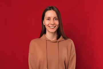 Simple studio portrait of a young wide smiling woman over dark red background.