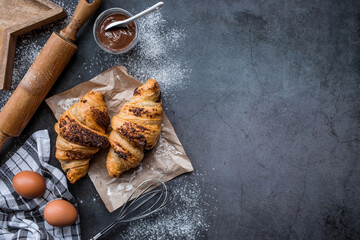 Delicious freshly baked croissants with chocolate, towel, wooden rolling pin and flour on a dark background. Bbreakfast. The context of a bakery with delicious bread.