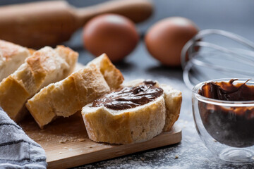 Delicious freshly baked baguette with chocolate on a dark background. French breakfast. Delicious pastries close-up. The context of a bakery with delicious bread. Confectionery products.