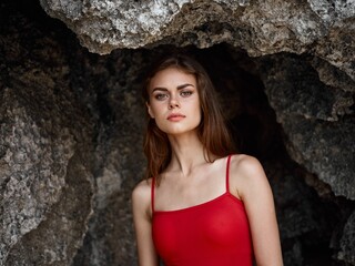 Portrait of a woman in a red swimsuit against the rocks by the ocean, tanned skin from the sun, the concept of protecting skin from the sun and body health