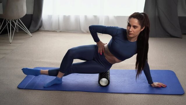 Athletic woman in a blue suit doing fascia exercises on the floor using a massage foam roller a tool to relieve tension in the back and relieve muscle pain