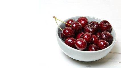 Sweet cherries in a ceramic bowl on wooden background, closeup. Fresh ripe sweet cherries in a bowl with droplets of water