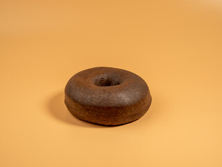 Fresh dark vegetarian donut on orange background. Close-up.