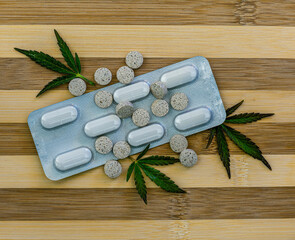 Fototapeta na wymiar medical green cannabis leaves with pills on brown wood background, green medicine marijuana with tablets and supplement