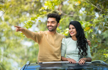 Happy smiling man showing nature to girlfriend on car sunroof at outdoor - concept of togetherness,...