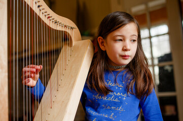 A young girl plucks at strings of small harp indoors