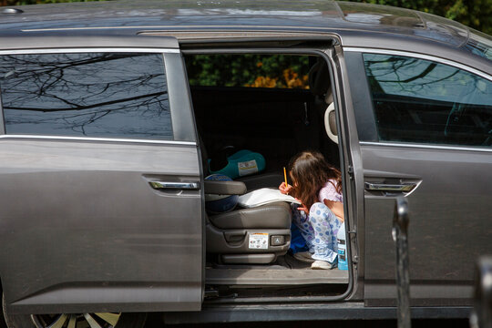A small child sits in open van drawing with pencil and paper