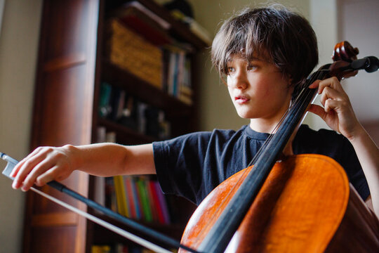 Close-up of serious child practicing cello in window light