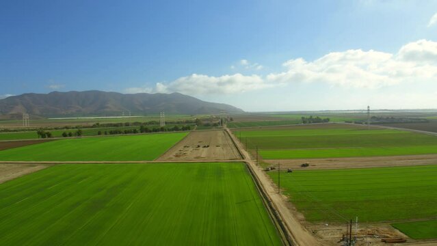 Aerial Panning Shot Of Green Agricultural Landscape By Mountains Against Cloudy Sky, Drone Flying Forward On Sunny Day - Camarillo, California