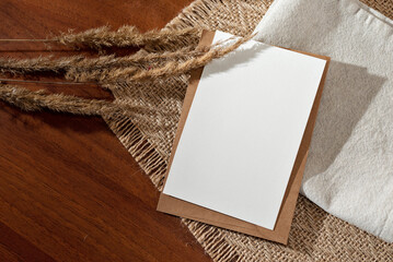 Blank paper card and dried meadow grass spikelets with floral shadows on wooden table, minimalist...