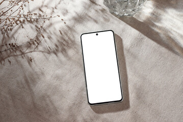 Mobile phone with blank screen mock up on neutral beige linen background with aesthetic floral sunlight shadows, minimalist business brand, social media blog template, copy space