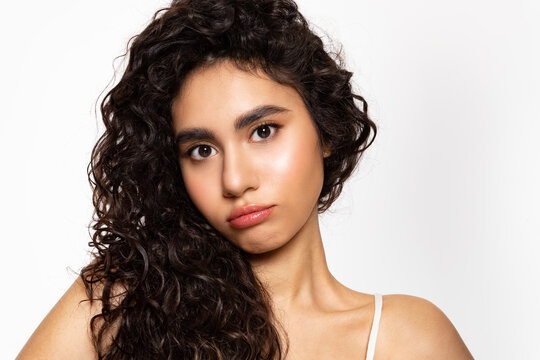 A beautiful girl with black curly hair and clear glowing skin makes a disgruntled face. A frustrated young woman looks at the camera and pouting lips.