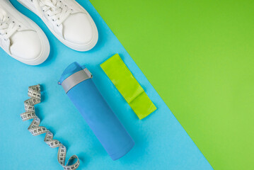 Sports concept. Top view photo of white sneakers of sports bottle elastic band and measuring tape on blue green background