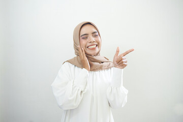 Cheerful beautiful Asian woman in white dress pointing fingers aside at copy space isolated over white background