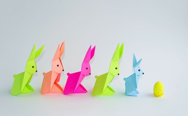 Multi-colored Easter rabbits made of paper, origami on a light background.  The concept of the holiday of Easter, the race for Easter eggs.  Front view, background image.