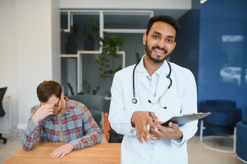 Fototapeta premium Indian doctor in white gown seeing patients in office.