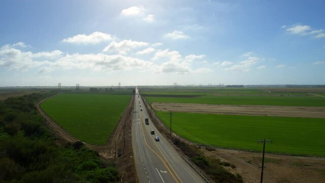 Aerial Panning Shot Of Vehicles Moving On Road During Sunny Day, Drone Flying Over Green Agricultural Landscape Against Clouds - Camarillo, California