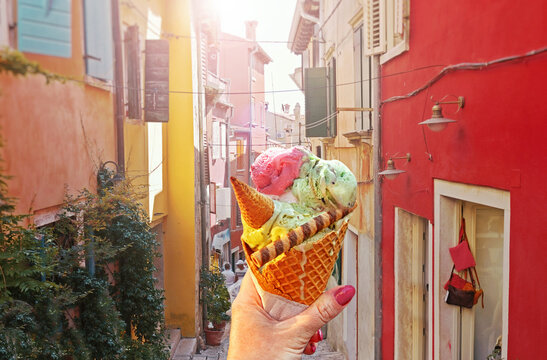 Woman hand hold  beautiful bright sweet ice - cream cone with different flavors  held in hand on the background of old street  in  Rovinj .Rovinj is a tourist destination on Adriatic coast of Croatia