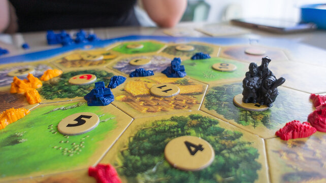 KRASNOYARSK, RUSSIA - JUNE 1, 2023:Board economic strategy game Settlers of Catan resources, build towns, cities and roads, robbers, bargain with neighbors on a wooden table for family game.  Catan