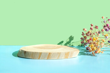 Wooden podium made of natural wood with flowers on a light green and blue background. Presentation of eco-products, layout