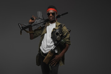 Studio shot of joyful military man of african ethnic with red headband and rifle.