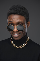 Obraz premium Joyful guy of african ethnic with chain and sunglasses isolated on grey background.