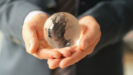 Businessman in suit holding glass globe with world map closeup. International financial relations...