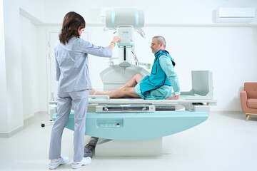 Female doctor preparing machine for medical scan of man knee