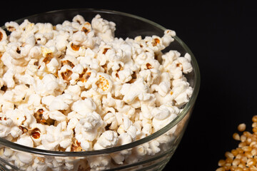 A bowl of fried popcorn and corn kernels on a black background