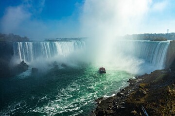 Fototapeta premium Aerial shot of Niagara Falls and a cruise going closer into steam, Ontario, Canada