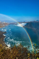 Vertical aerial shot of Niagara Falls and a rainbow above it under the blue sky, Canada