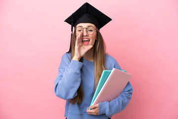Young student woman wearing a graduate hat isolated on pink background shouting with mouth wide open