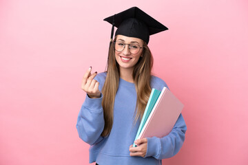 Young student woman wearing a graduate hat isolated on pink background making money gesture