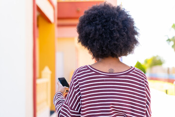 Fototapeta premium African American girl using mobile phone at outdoors in back position