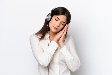 Fototapeta premium Telemarketer caucasian woman working with a headset isolated on white background making sleep gesture in dorable expression