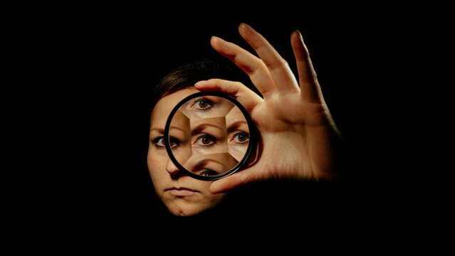 woman looking through a magnifying lens at herself on a black background