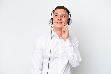 Telemarketer Brazilian man working with a headset isolated on white background thinking an idea while looking up