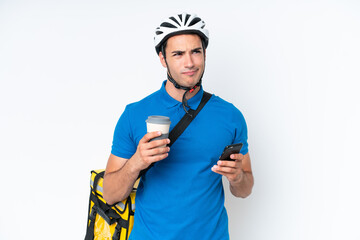 Young caucasian man with thermal backpack isolated on white background holding coffee to take away and a mobile while thinking something