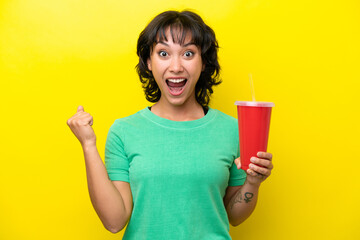 Young Argentinian woman holding a soda isolated on yellow background celebrating a victory in winner position